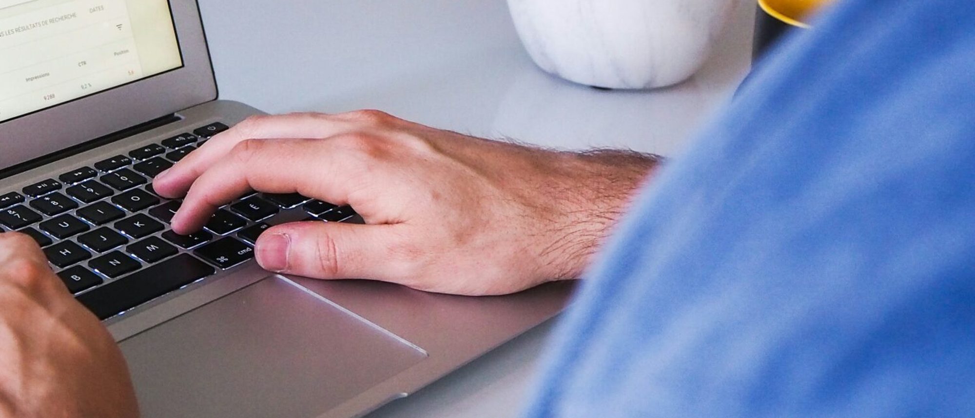 Mains qui tapent sur le clavier d'un ordinateur portable, sur un bureau clair